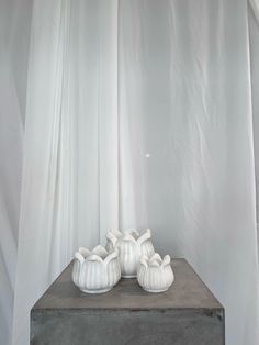 two white ceramic vases sitting on top of a wooden table next to a curtain