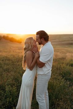 a man and woman kissing in the middle of an open field with sunset behind them