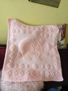 a pink crocheted blanket sitting on top of a pillow