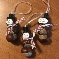 three ornaments made to look like snowmen hanging from strings on a wooden table top