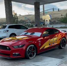 a red car is parked in front of two white cars at a gas station with lightning bolt painted on the side