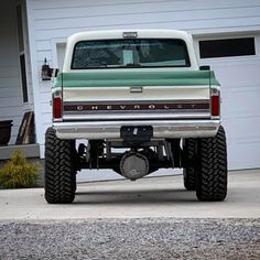 a green and white pickup truck parked in front of a garage with its flat tire