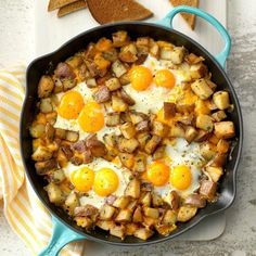 a skillet filled with eggs and potatoes on top of a white table next to bread