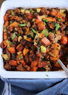 a white casserole dish filled with meat and veggies on top of a blue towel