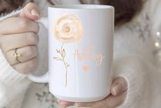 a woman holding a white coffee mug with an orange and pink flower on it's side