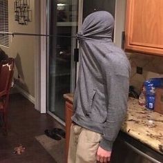 a person standing in the kitchen looking at something on the floor behind them and wearing a hood over their head