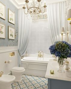 a white bathroom with blue and gold decor on the walls, chandelier over the bathtub