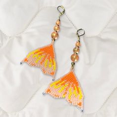 two orange and yellow beaded butterfly earrings on a white surface with beads hanging from them