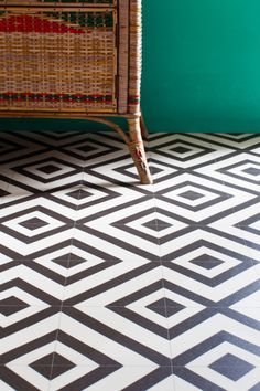 a wicker chair sitting on top of a black and white tiled floor next to a green wall