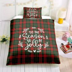 a bed covered in a plaid comforter with the words tis the season to be jolly on it