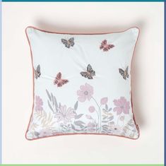 a white pillow with pink flowers and butterflies on it, against a light blue background