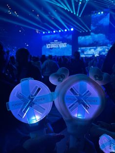 people are sitting in the audience at an event with blue lights on their head and mickey ears