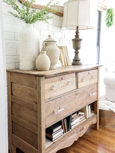 a wooden dresser with books and vases on it in a white living room area