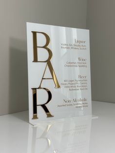 a bar sign sitting on top of a white counter next to a wall with gold lettering