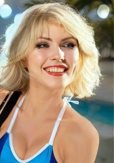 a woman with blonde hair wearing a blue top and white bra smiling at the camera