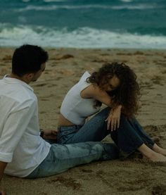 a man and woman sitting on the beach next to each other