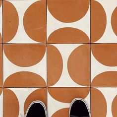 a pair of black and white shoes sitting on top of a tiled floor with circles