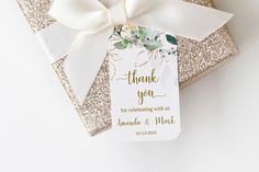 a gift wrapped in gold glitter with a white ribbon and tag that says thank you for celebrating with us