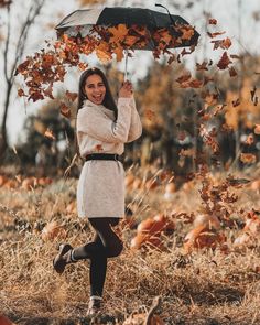 a woman is holding an umbrella in the air while walking through autumn leaves and grass