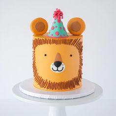 a birthday cake with a lion face on it's side and a party hat on top