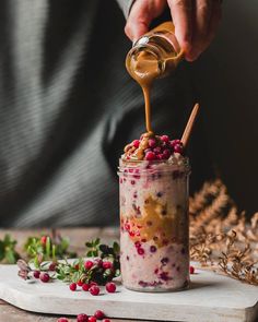 a person is pouring something into a jar with berries on it and sprinkled with caramel