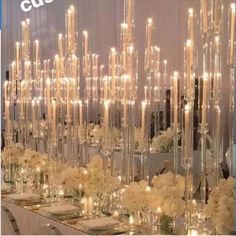 a table topped with lots of white flowers next to tall vases filled with candles