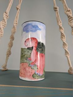 a mug with a dinosaur painted on it sitting on a table next to roped ropes