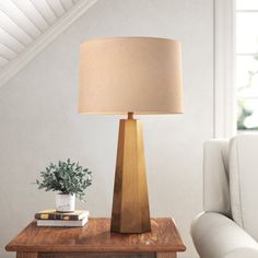 a wooden table with a lamp on top and a book next to it in front of a white couch