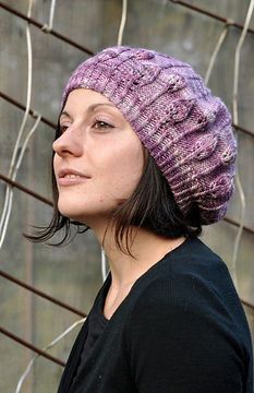 a woman wearing a purple knitted hat standing next to a wire fence and looking off into the distance