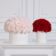 two white vases with red and pink flowers on top of each one, sitting side by side