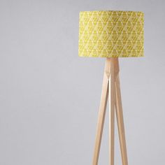 a wooden tripod floor lamp with a yellow lampshade on the top and bottom