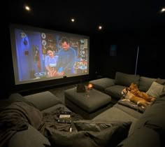 a dog laying on the couch in front of a large screen with two people watching