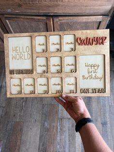 a person holding up a wooden frame with words on it that say hello world and happy 1st birthday