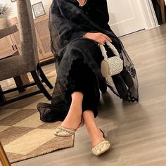 a woman sitting on the floor with her legs crossed wearing slippers and a black dress