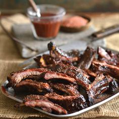 barbecue ribs on a plate with sauce and spoons in the background, ready to be eaten