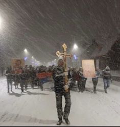 a man holding a cross in the middle of a snow storm with people standing around him