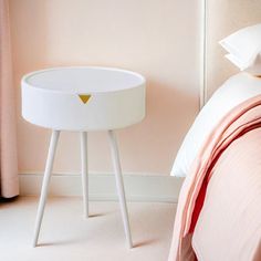 a white table sitting on top of a bed next to a pink comforter and pillows