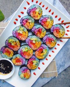 colorful sushi on a plate with dipping sauce and chopsticks next to it