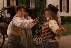 two children are dancing in front of a horse drawn buggy on the street while another child holds his hand out