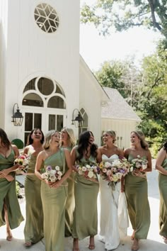 a group of women standing next to each other in front of a church with bouquets