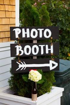 a wooden sign that says photo booth with an arrow on it and flowers in front