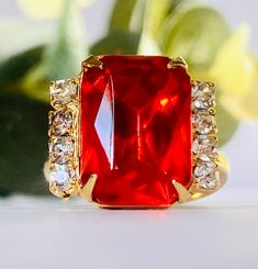 This vintage ring features a gold tone adjustable band with a prong set red rhinestone center flanked by clear stones. The ring is fairly lightweight and it is comfortable to wear. Overall, very good vintage condition. FREE SHIPPING OVER $35 MAKE AN OFFER AVAILABLE ON ALL LISTINGS Please be aware that we are not jewelry experts. We have a sincere love of all things vintage especially vintage jewelry. We hope to share our finds with you. That being said, we describe our items to the very best of our ability. Please view all photos and know that each phone or computer screen may display slightly different colors. Please ask any and all questions. We gladly accept returns and provide shop credit or refund upon receiving the item back. The buyer pays return shipping unless the item is grossly Red Jeweled Rings As Gift, Red Vintage Crystal Promise Ring, Vintage Red Crystal Wedding Ring, Vintage Red Crystal Promise Ring, Vintage Red Diamond Ring For Gift, Vintage Red Crystal Ring For Wedding, Gold Ruby Crystal Ring With Prong Setting, Luxury Retro Red Jewelry, Vintage Red Jewelry With Brilliant Cut