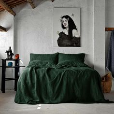 a bed with green sheets and pillows in a room next to a painting on the wall