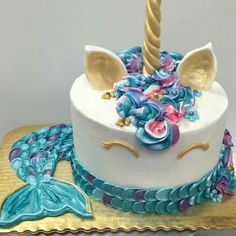 a white cake decorated with blue and pink icing has a unicorn horn on top