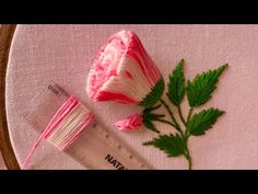 a pink and white flower sitting on top of a table next to a measuring tape