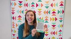 a woman holding up a book in front of a quilt