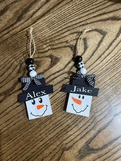 two snowman tags are hanging on a wooden table with the words alex and jack attached to them