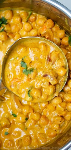 a ladle full of chickpeas and carrots is being stirred by a spoon