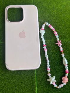 a cell phone with a beaded necklace next to an iphone case on the grass