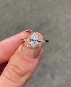 a woman's hand holding an engagement ring with a pear shaped diamond on it